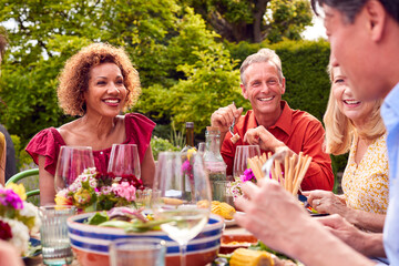 Group Of Mature Friends Talking Around Table At Summer Dinner Party In Garden At Home