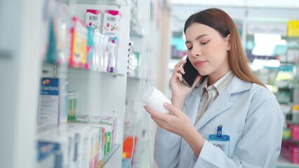 Professional asian woman pharmacist helping customer with medicine recommendation talking with customer on smartphone in drugstore