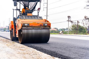 Machines are crushing the asphalt after pouring to make a road for cars.