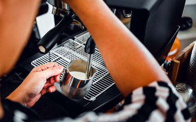 Hand of a barista in the coffee shop preparing and using a coffee machine to steam milk for a coffee menu.