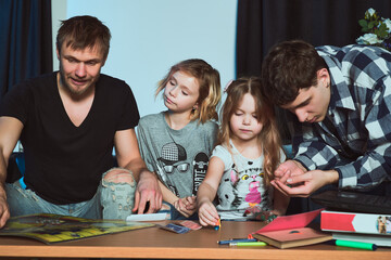 Staged photo. Homosexual couple and their children, two cute girls, at home. One of the parents helps the girls figure out the rules of the game.