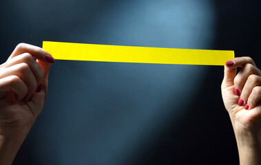 Hands holding yellow tape stripe with place for your text on a dark background. Warning and danger concept.