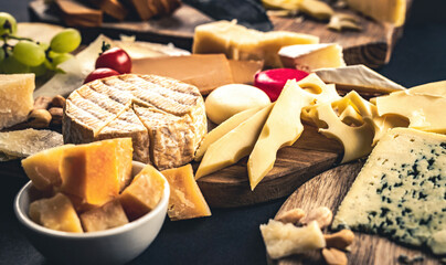 Different kinds of cheese on wodden plate table served with grape and tomato. Organic parmesan,...