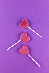 Three pink candies on stick in shape of a heart on purple background