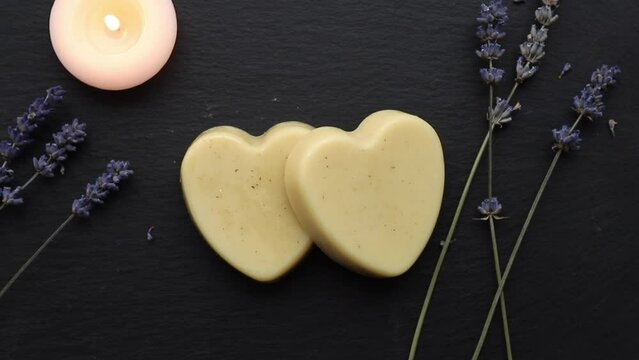 Handmade beeswax and shea butter solid moisturizing hand cream. Heart shape cream bar made of all natural ingredients. Background with dried lavender flowers and candle burning.