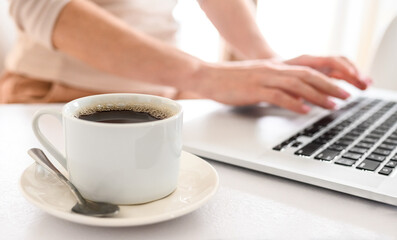 Girl typing on a laptop keyboard and drinking a coffee