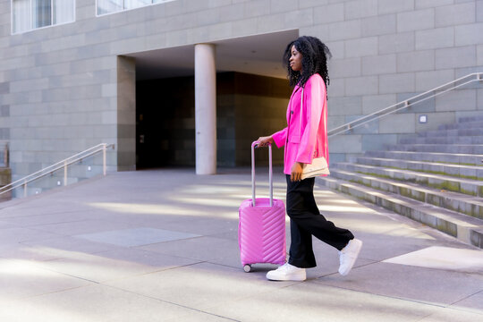 African american young woman in the city, portrait of a young woman in pink jacket walking with a suitcase