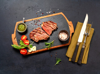 Fototapeta na wymiar Grilled ribeye beef steak, chimichurri sauce, herbs and spices on a dark table. Sliced steak on dark board for steak