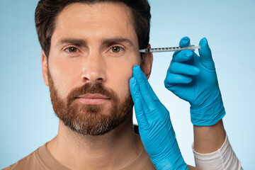 Closeup shot of handsome bearded man getting filler for eyes zone at beauty salon or aesthetic...