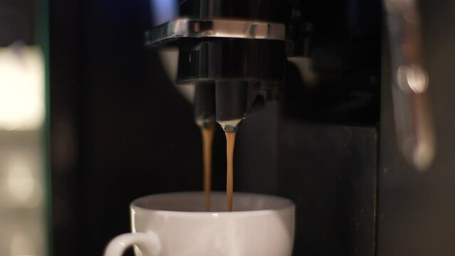 Close up of coffee machine filling cup. Close-up of pouring coffee stream from machine in cup. Home making hot espresso coming out from automated coffee maker machine. Flowing fresh ground coffee.