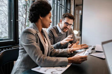 A multiracial businesspeople are sitting at the boardroom and having discussion about project. They...