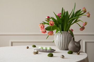 Minimalist composition of easter dining room interior with round table, vase with tulips, bowl with...