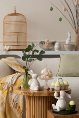 Spring composition of living room interior with round coffee table, beige sofa, easter bunny...
