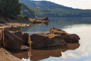 lake surrounded by green forest, hill with forest on background.Summer day.Large rock in water