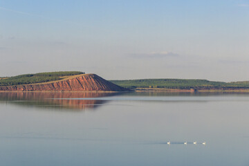 lake with a red hill with forest in the background, red hill with forest on background