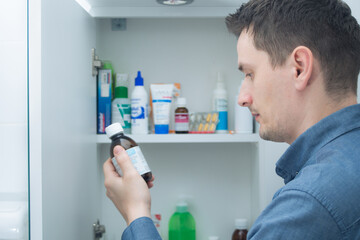 Man hold medication bottle reading instruction or prescription on packaging. Man looking at bottles from medicine cabinet - Powered by Adobe