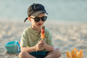 Little charming boy eating ice cream on the beach on vacation. Summer holidays near the see. Happy...