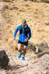 Young man practising trail running in the high mountains, while climbing to the top of the mountain.