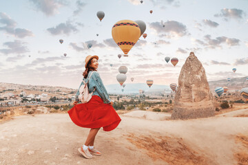 Young girl in a red dress stood in awe as she watched vivid air balloons ascend into the sky in...