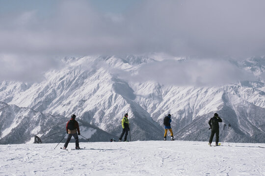 Skiers and snowboarders on ski slope preparing for riding against the backdrop of stunningly beautiful mountain peaks in clouds