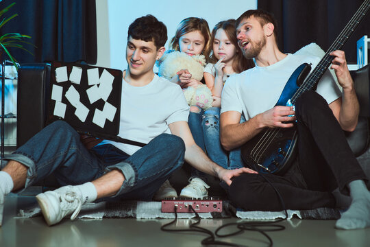 Staged photo. Homosexual couple and their children at home. The whole family is gathered on the couch. One of the parents is tuning the guitar. Well, does anyone have an ear for music in this family?