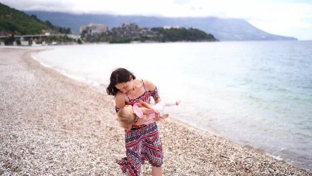 Mom sways a little girl in her arms while standing on a pebble beach