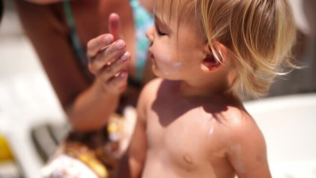 Mom smears sunscreen on the face and shoulders of a little girl