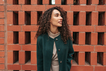 Portrait of young woman in green coat with curly hair in the city