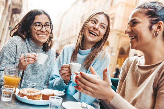 Three young women enjoying breakfast drinking coffee sitting at bar cafeteria - Life style concept with female friends hanging out on city street - Food, beverage and friendship concept