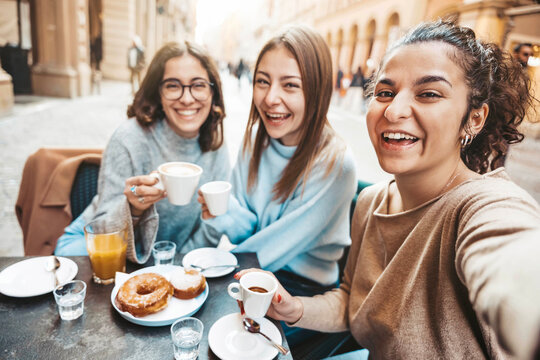 Three young women taking selfie picture drinking coffee sitting at bar cafeteria - Life style concept with female friends hanging out on city street - Food, beverage and friendship concept