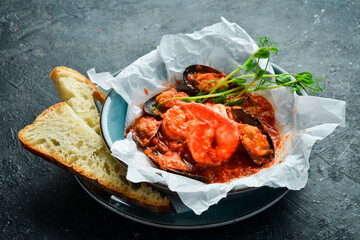 Seafood. Shrimps and mussels cooked in tomato sauce, served with croutons. On a black stone background.