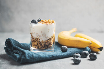 Granola cereal oatmeal with white yogurt, blueberries and banana fruits in a glass on a blue...