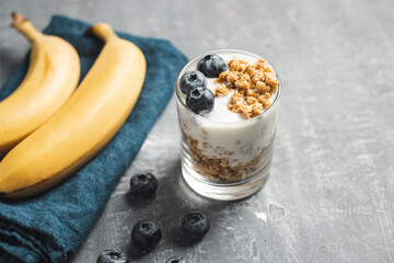 Granola cereal oatmeal with white yogurt, blueberries and banana fruits in a glass on a blue...