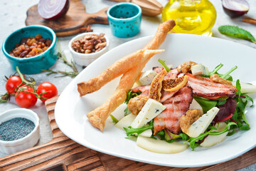 Salad with bacon, blue cheese and figs, served with grissini. On a white plate. On a gray stone background. Restaurant menu.