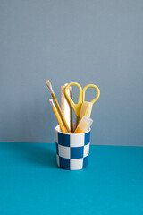 Yellow pencil, ruler, highlighter, scissors in holder on blue desk