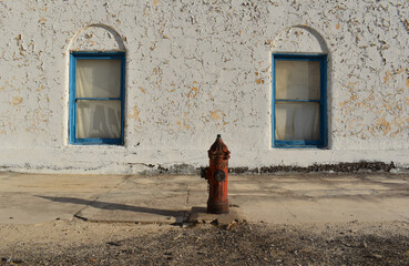 Old red fire hydrant against the backdrop of peeling paint on the wall with two blue framed...