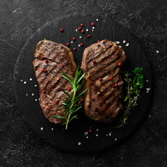 Two juicy rib eye steak, herbs and spices. On a black stone background.