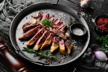 Chopped juicy porterhouse steak or T Bone Steak dry aged of beef Ready to Cook on wooden Board with herbs, pepper and salt. On a black stone background.