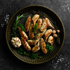 Grilled sausages with rosemary and spices. Barbecue. On a black stone background.