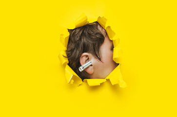 Close-up of a male ear with a dollar rolled into a tube through a torn hole in yellow paper. The...