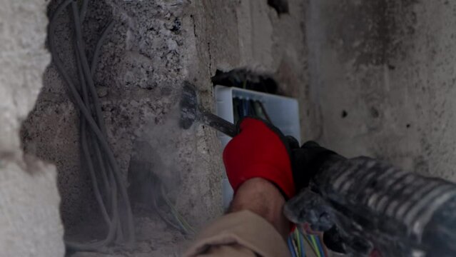 The worker is preparing wall with jackhammer for installing an electrical box, close-up 4k video.