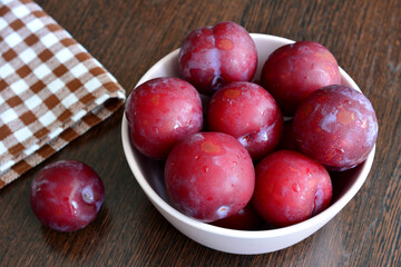 bowl with purple garden plums isolated on dark wooden kitchen table, macro