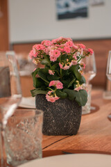 Flores color rosa en un macetero oscuro encima de una mesa de madera de un restaurante con vasos desenfocados alrededor