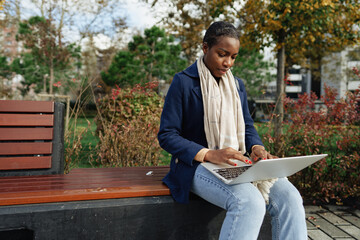 Obraz premium Young african businesswoman using laptop while sitting on the bench in the city