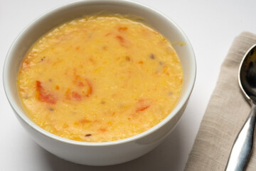 Homemade yellow split pea and mung soup,  with onions and tomato,es , served in a white bowl on a white background. Close-up.