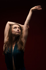 Cute girl against dark red background. Brunette lady wearing fancy shirt with hands up looking up.