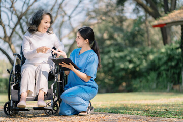 young woman in blue workwear nurse helping senior woman in wheelchair with questionnaire, asian pensioneer filling papers at nursing home, having assistance.