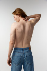 Rear view photo of young man posing shirtless in jeans over grey studio background. Moles on body, healthy strong back, spine. Concept of men's health, body and skin care, hygiene and male cosmetology