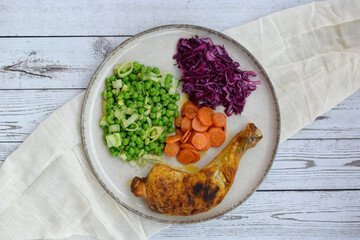 Roasted chicken leg served with vegetables on a plate, top view