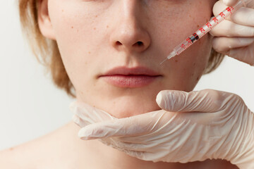 Young redhead man having cosmetological injections. Male model posing against grey background. Lip...